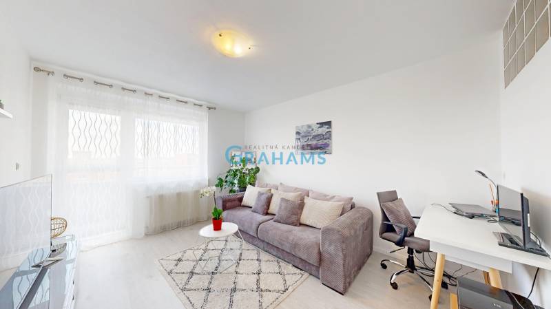 Obývačka v 2-izbovom byte s pohodlnou sedačkou, pracovným stolom a veľkým oknom.